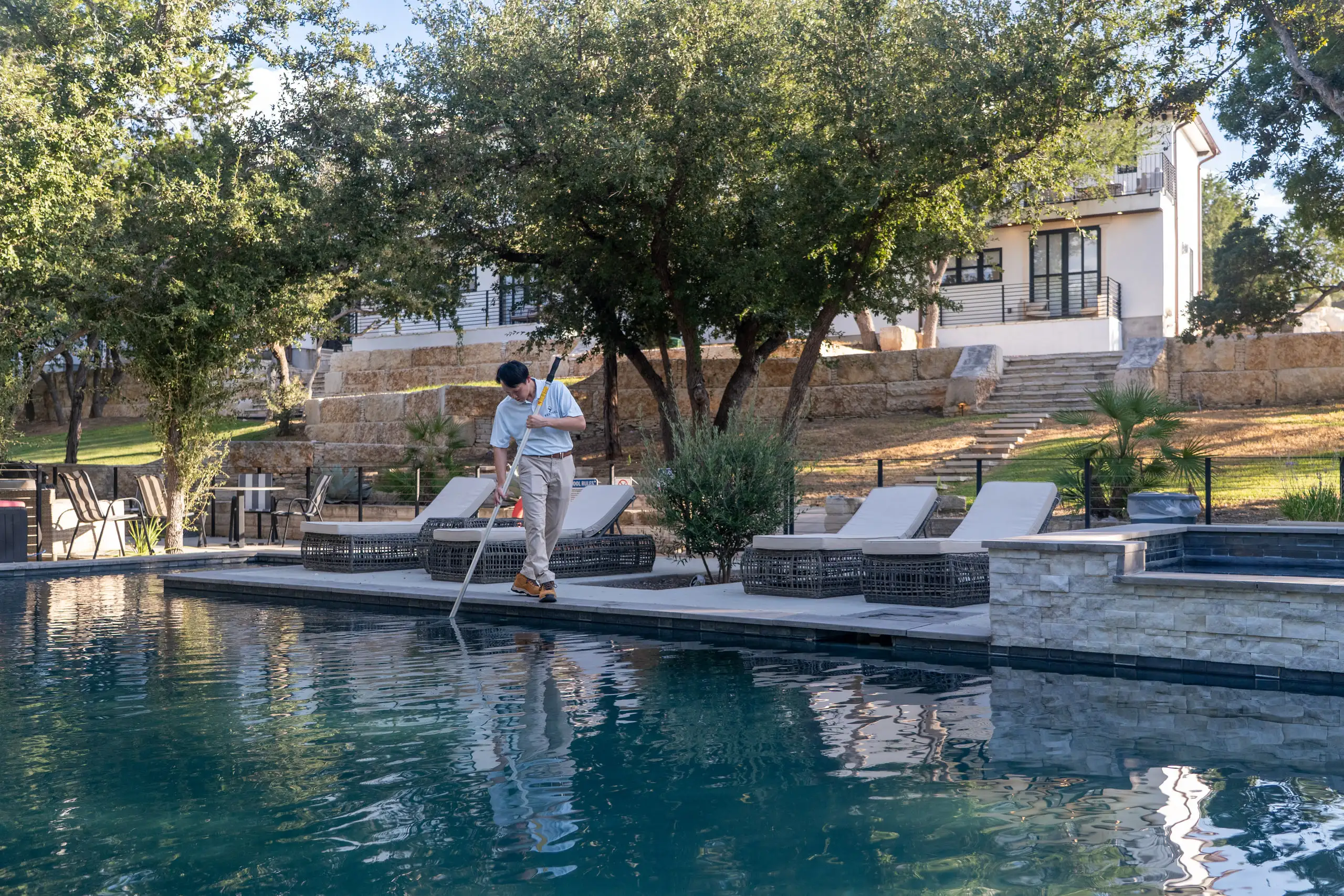 Ji brushing the edge of a West Austin pool on a live-oak-shaded deck, the house on the terrace behind him