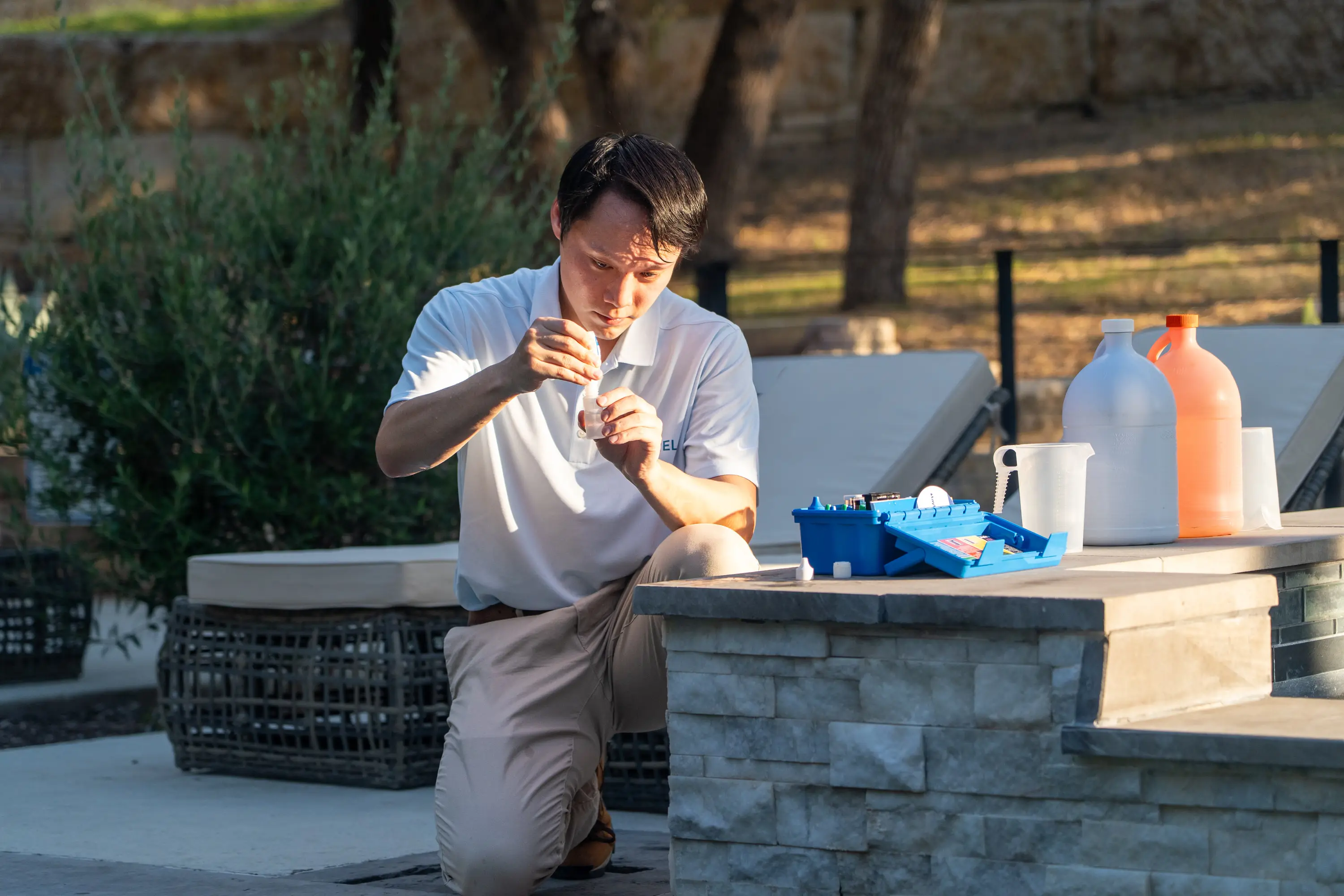 Ji adding reagent to a test vial, with an open test kit, beaker and chemical bottles on the pool ledge beside him